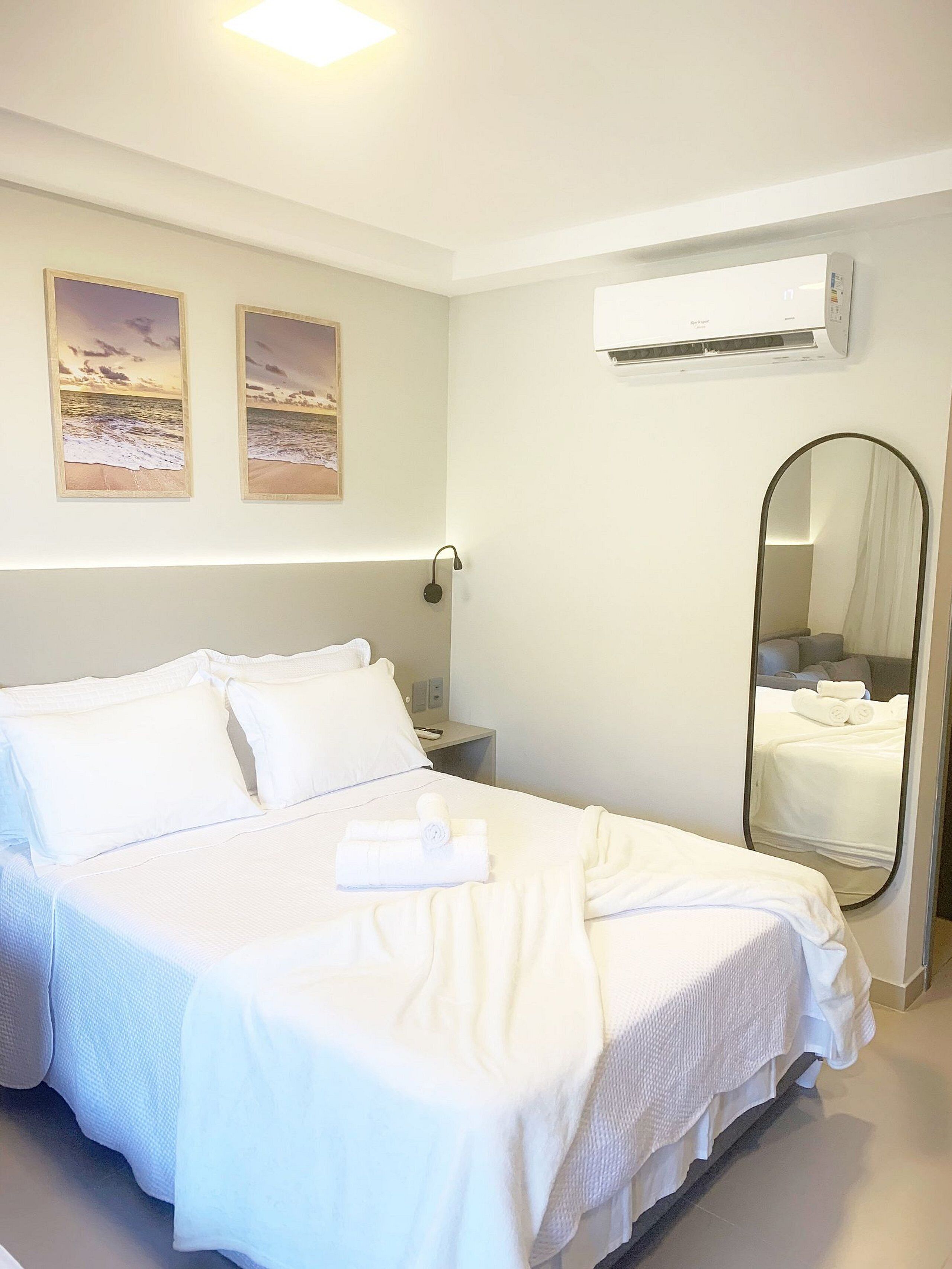 A hotel room with a bed, a nightstand, a mirror, and two framed pictures on the wall.