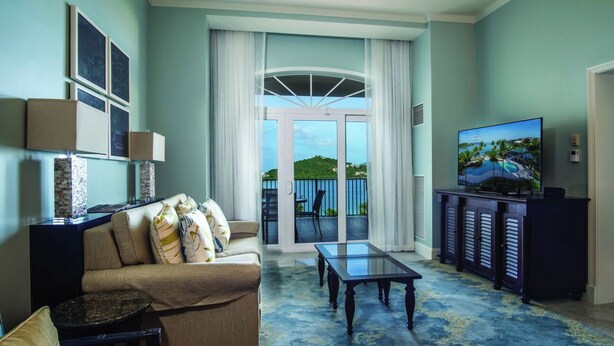 Un salon comprenant un canapé, une table basse, un téléviseur et un balcon donnant sur un espace verdoyant.