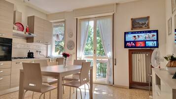 Eine moderne Küche mit Essbereich, einem an der Wand befestigten Fernseher und Blick ins Freie durch große Fenster.