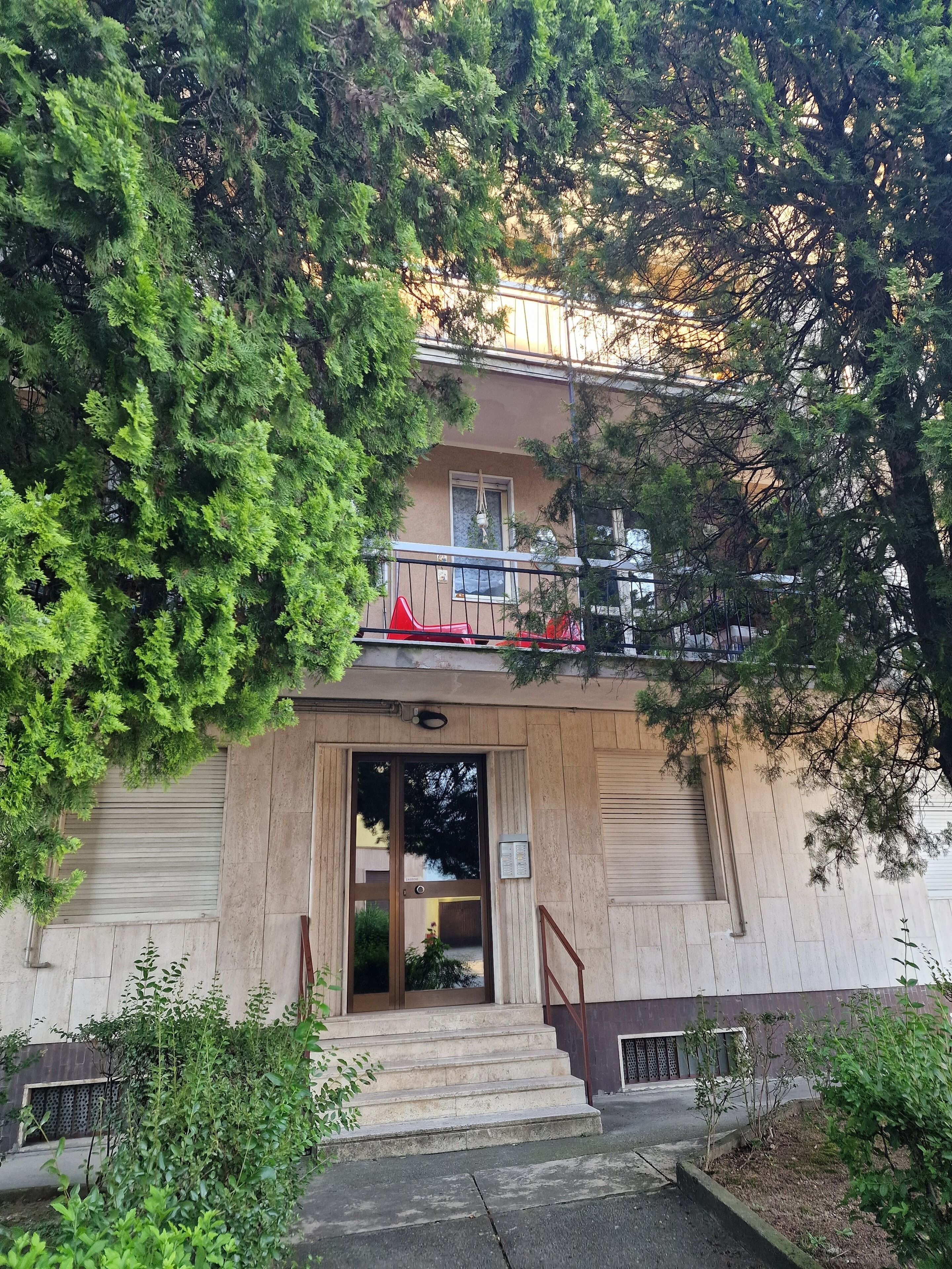 Ein Gebäude mit Holzfassade, einem sichtbaren Eingang und einem kleinen Balkon mit roten Stühlen.