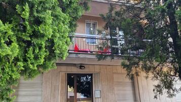 Ein Gebäude mit Holzfassade, einem sichtbaren Eingang und einem kleinen Balkon mit roten Stühlen.