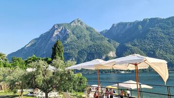 Eine Seeterrasse mit Liegestühlen und Sonnenschirmen, mit Blick auf einen See und Berge.