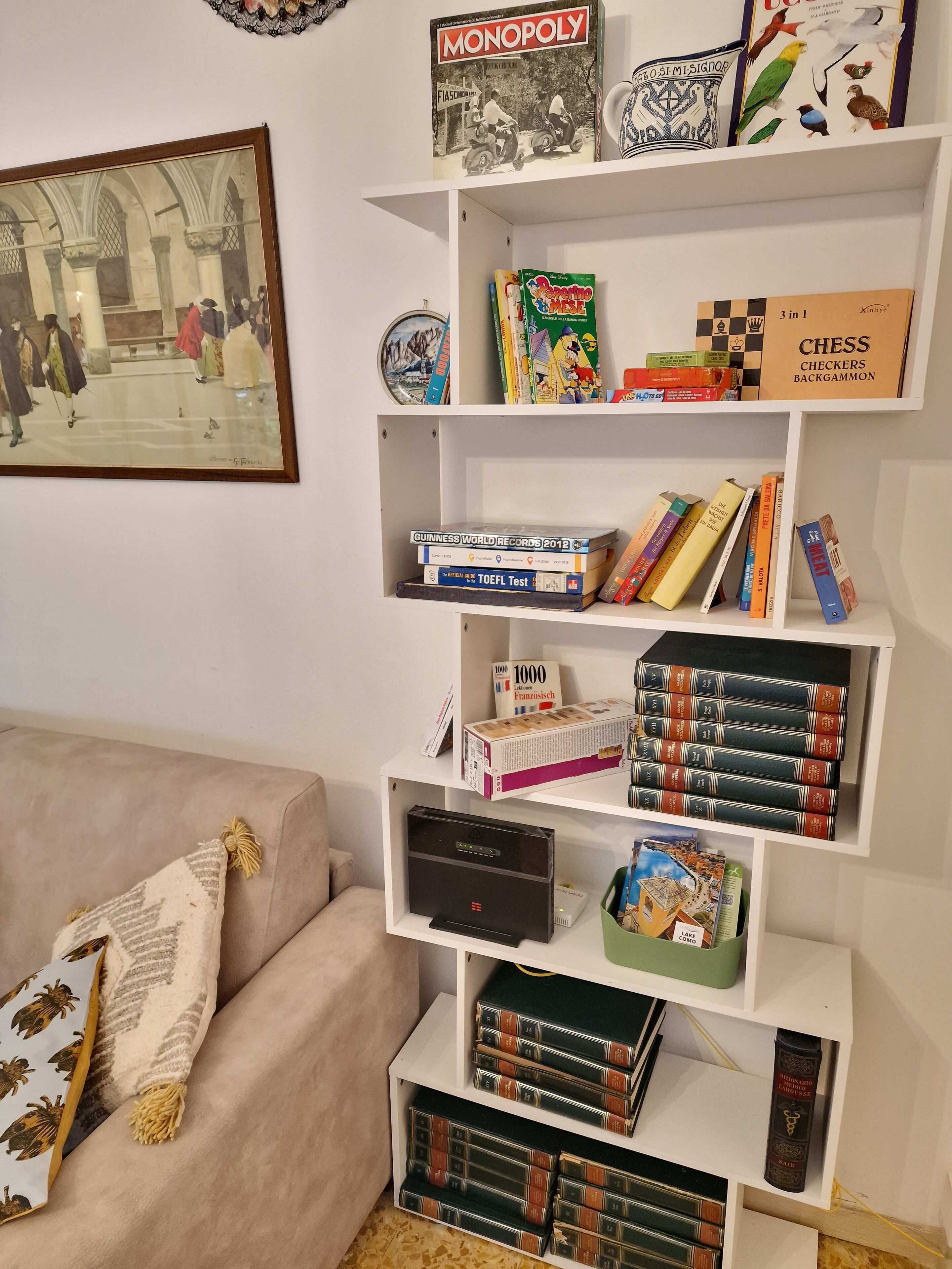 A bookshelf with various board games, books, and a framed painting.