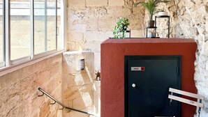 Uma escadaria com parede vermelha, porta preta com o letreiro 'PRIVÉ', uma janela e um banco.