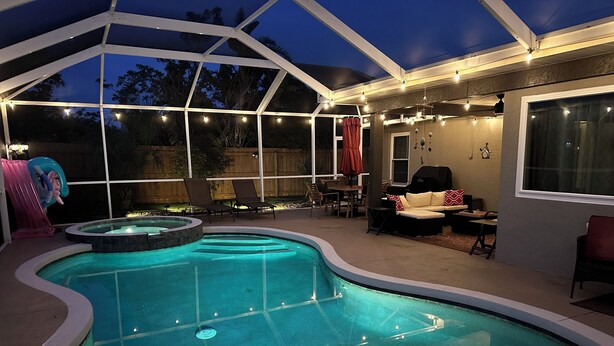 A swimming pool with a hot tub, surrounded by lounge chairs and a covered patio area with string lights.