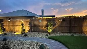 A residential backyard with a wooden fence, a paved patio, and a lawn.