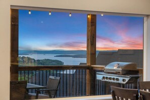 A balcony with a view of a sunset over water, a grill, and wicker furniture. - On The Rocks - Home for 16! (Branson)