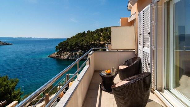 Ein Balkon mit Korbmöbeln, einem kleinen Tisch mit Obst und Blick auf das Meer sowie eine felsige Küstenlinie.
