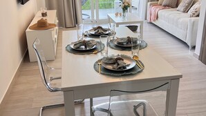 Een moderne eetruimte met een tafel voor vier personen, transparante stoelen en een bank op de achtergrond.