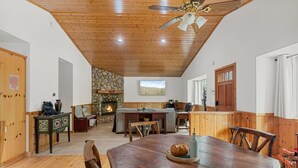 A cozy room with a stone fireplace, wooden ceiling, and a dining table with chairs.