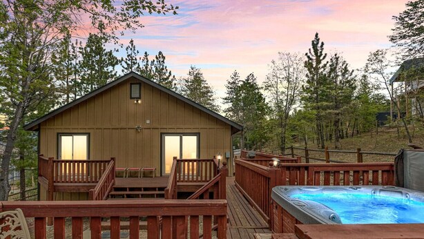 A wooden cabin with a hot tub and deck, surrounded by trees.