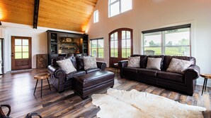 Ein großzügiges Wohnzimmer mit Ledersofas, Holzboden und großen Fenstern mit Blick ins Freie.