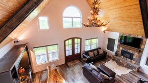 Ein geräumiges Wohnzimmer mit Kamin aus Stein, Ledersofas und Holzbalkendecke.