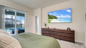 A bedroom with a large bed, a wooden dresser, and a sliding glass door leading to a balcony with outdoor furniture.