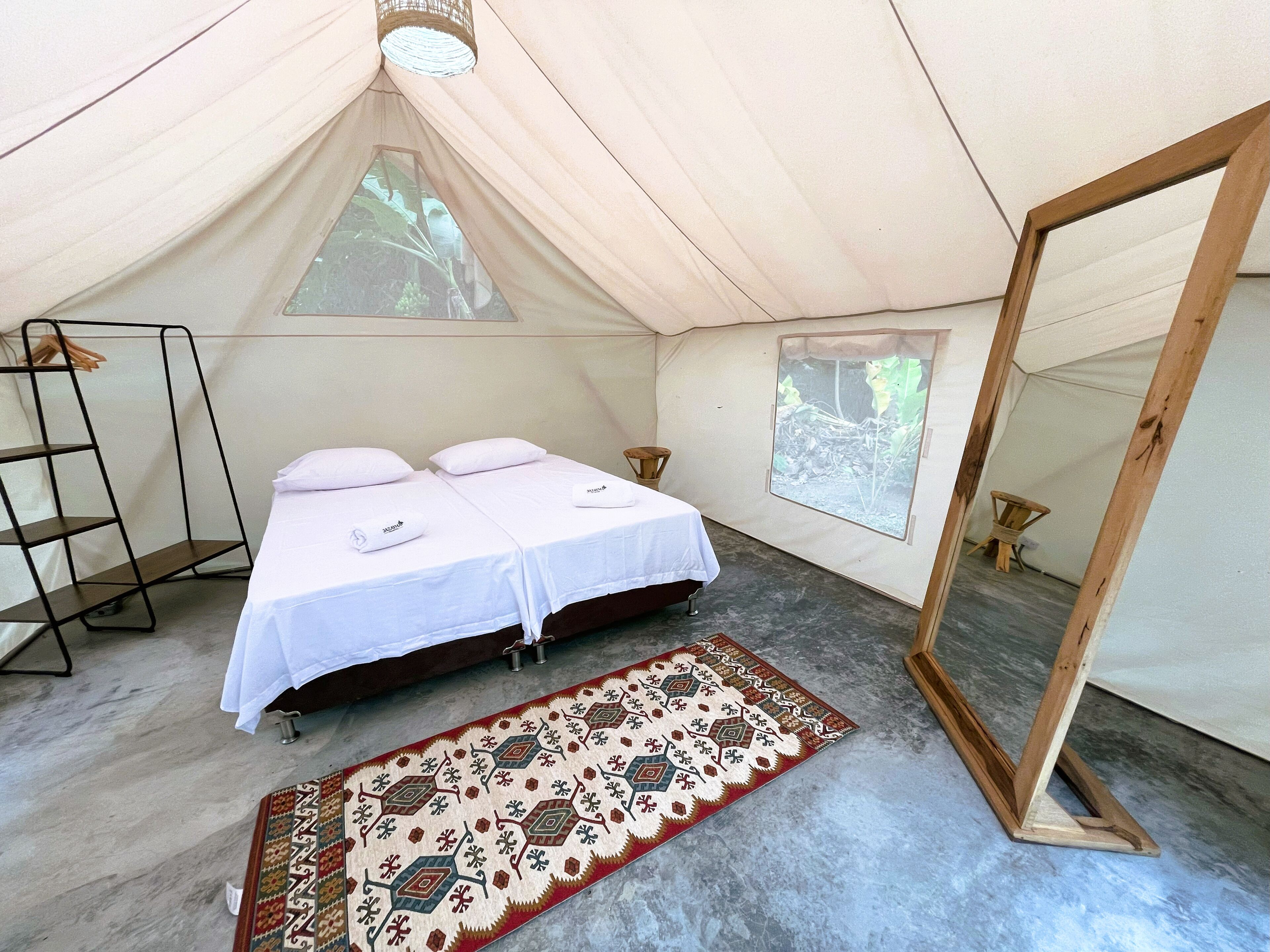 A tented accommodation room with two beds, a mirror, a wooden ladder, and a patterned rug.