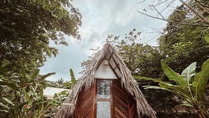 Uma cabana com telhado de palha, porta de madeira e degraus que conduzem a ela, rodeada por vegetação exuberante.
