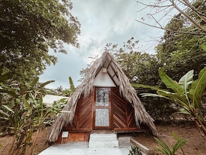 A thatched-roof hut with a wooden door and steps leading up to it, surrounded by lush greenery. - Glamping Kunna Tayrona (Santa Marta)