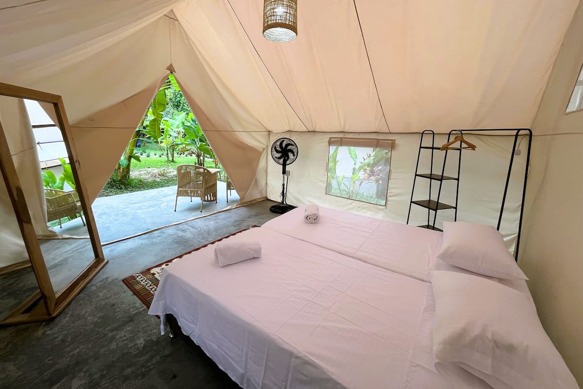 A tented accommodation with a bed, a fan, a window, and a chair.
