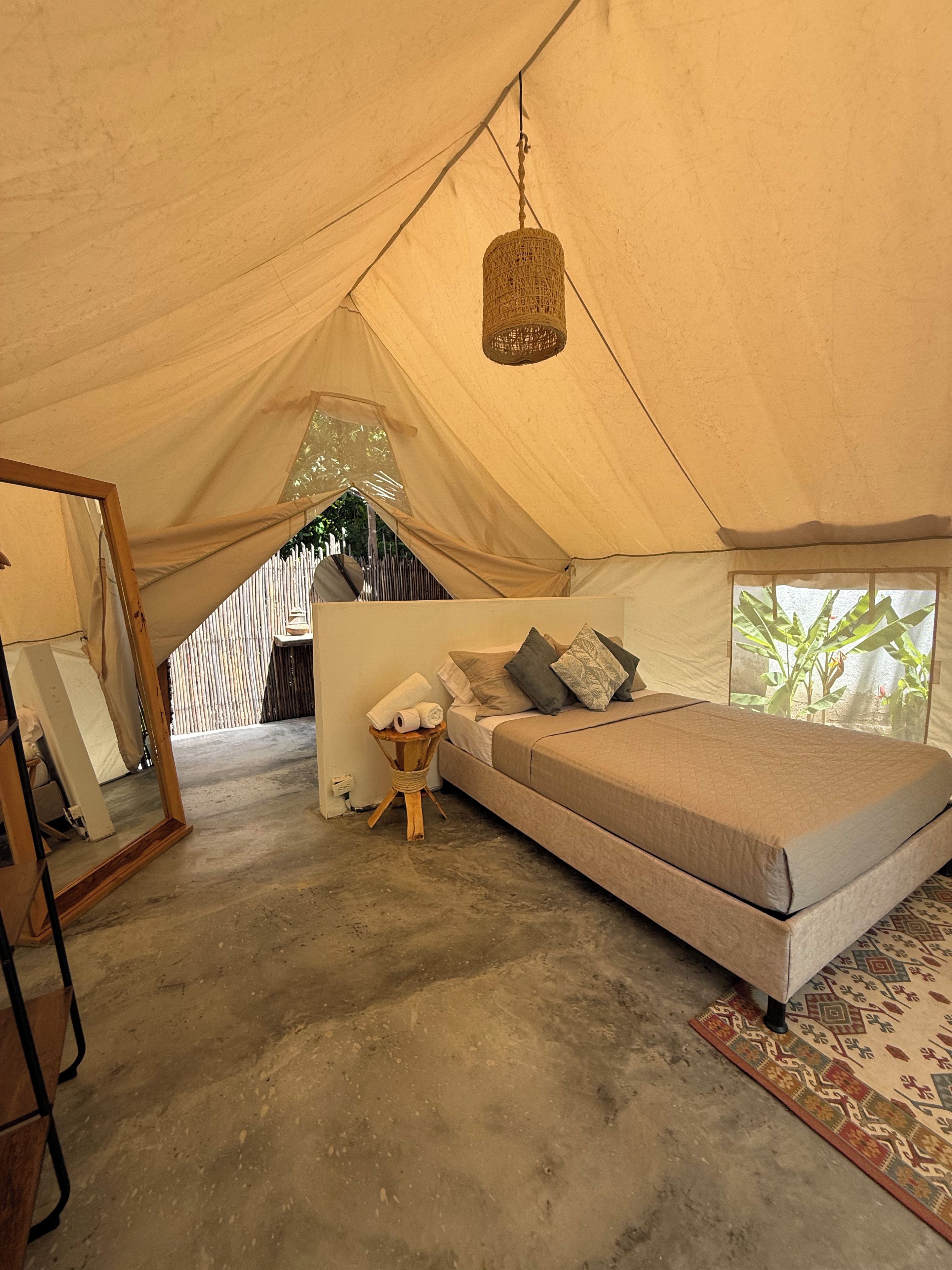 A tent with a bed, a hanging light fixture, and a small table with towels.