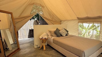 A tent with a bed, a hanging light fixture, and a small table with towels.