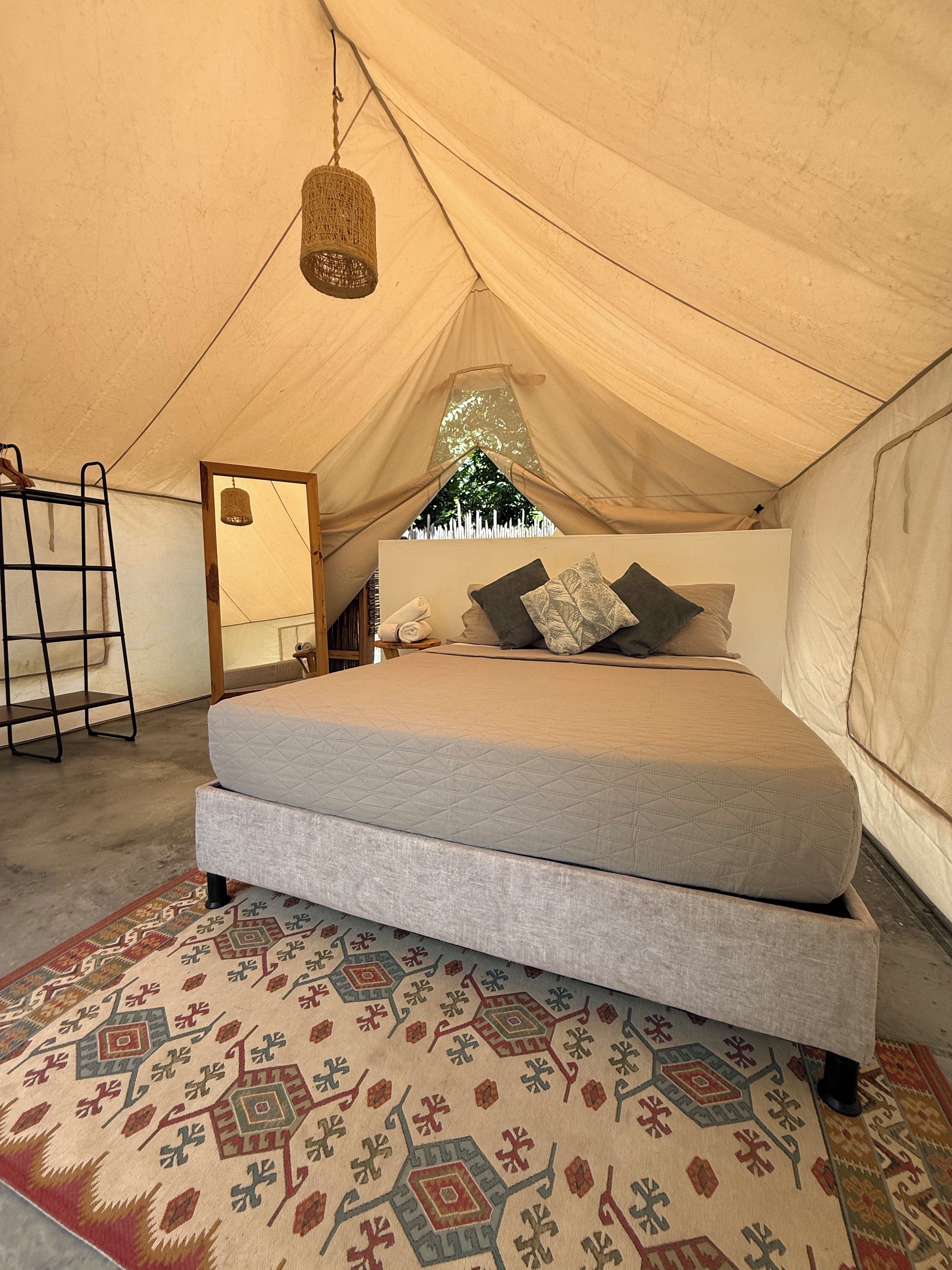 A tent with a bed, a hanging light fixture, and a patterned rug.