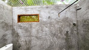 Un baño pequeño y rústico con una pared de concreto, una ventana con marco de madera, un inodoro y una zona de ducha.