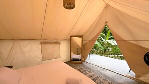 Habitación tipo tienda de campaña con cama, una lámpara colgante y vistas a la vegetación exterior.