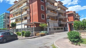 A multi-story residential building with balconies, a gated entrance, and a street in front.