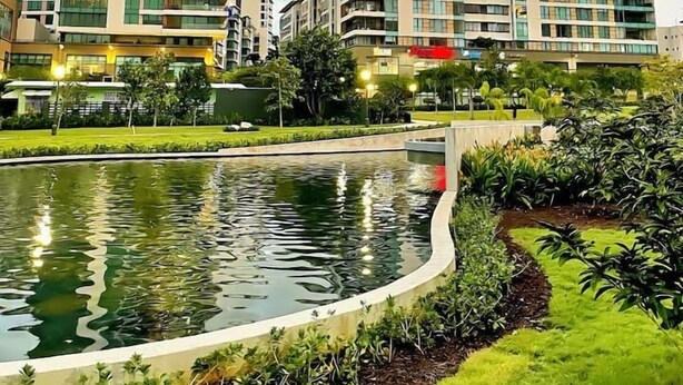 A modern building complex with multiple high-rise structures, a central water feature, and surrounding greenery.
