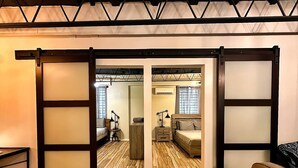 A room with a wooden floor, a bed, a desk, and a chair. There is a sliding door with frosted glass panels.
