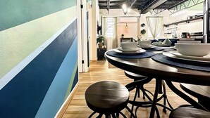 A modern kitchen with a striped wall, wooden flooring, and a dining area with a round table and stools. - Loft Living – Stylish & Central Santurce (San Juan)