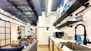 A modern kitchen with a wooden countertop, a black faucet, and a microwave. There is a striped rug on the floor and a gray sofa with orange cushions in the living area. - Santurce Skylight – Modern Lofts Stay (San Juan)