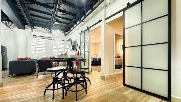 A spacious room with a wooden floor, a round table with chairs, and a sliding glass door leading to another room. - Santurce Skylight – Modern Lofts Stay (San Juan)