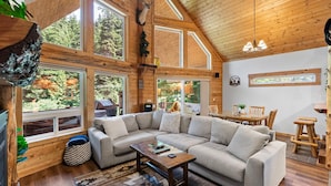 Amplia sala de estar con un sofá modular en forma de L, una mesa de centro de madera y vistas al bosque a través de grandes ventanales.