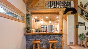 Una cocina con una isla de piedra, taburetes de madera y vista al piso superior.