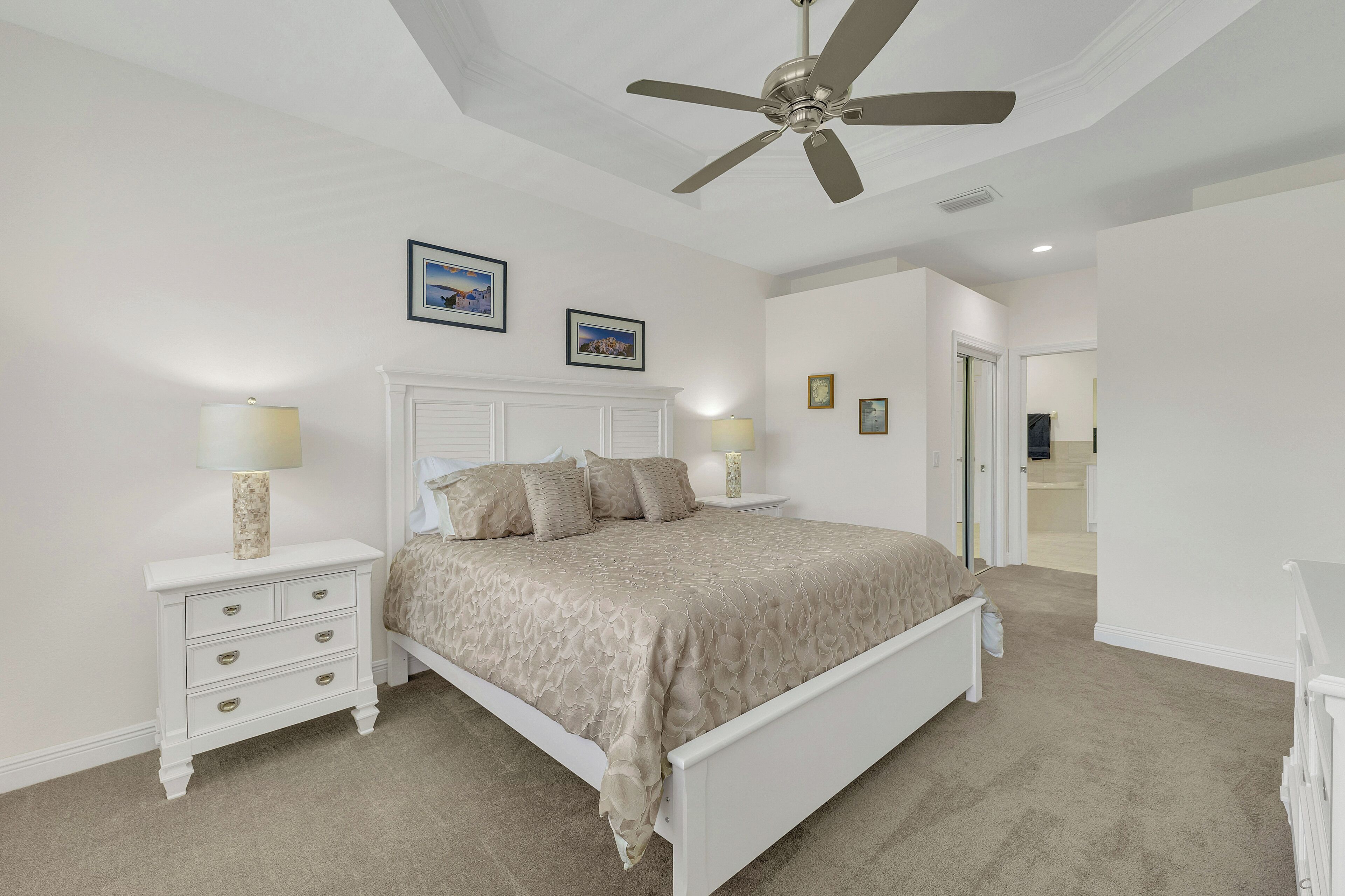 A bedroom with a bed, nightstands, a ceiling fan, and framed pictures on the wall.