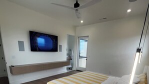 Un dormitorio moderno con una cama grande, ventilador de techo, televisor montado y puerta que da a un balcón.