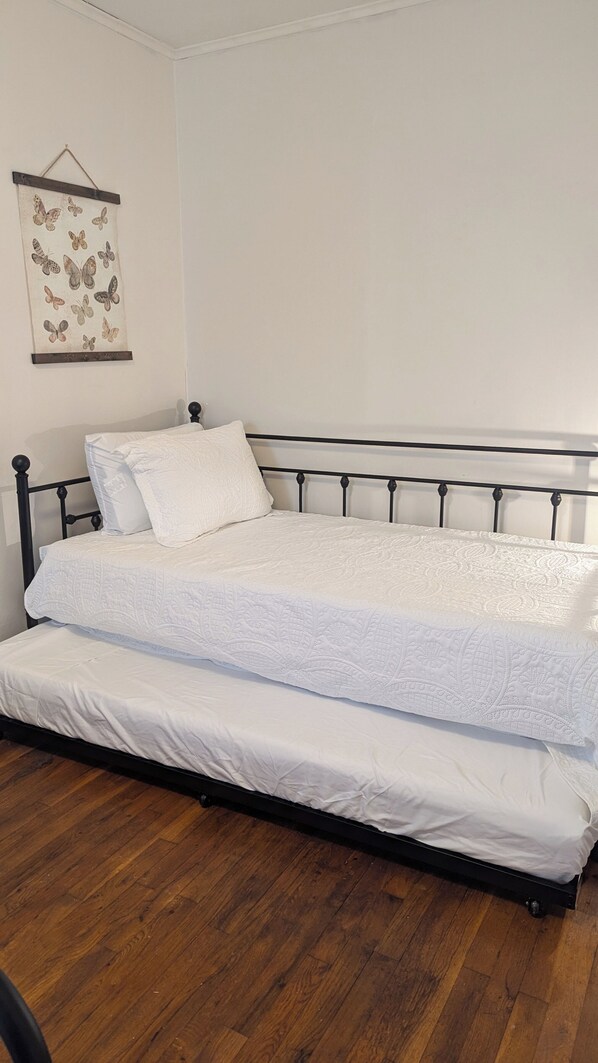 Un lit double avec une couette blanche, une tête de lit et un plancher en bois.