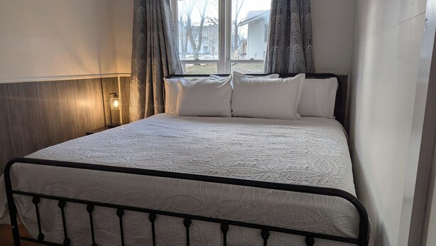 Ein Bett mit einem gemusterten Quilz, einer Nachttischlampe und Vorhängen mit Muster.