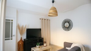 Een woonkamer met een flatscreen televisie, een bank, een salontafel, een decoratieve spiegel en een hanglamp.