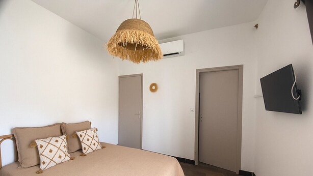 Een slaapkamer met een bed, twee deuren, een hanglamp en een tv aan de muur.