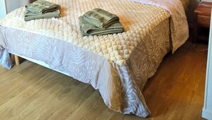 En snyggt bäddad säng med ett mönstrat överkast, en sänggavel med en vävd panel och ett trägolv.
