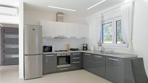 A modern kitchen with grey cabinets, a stainless steel refrigerator, a microwave, a stove, and a coffee maker. - Gorgeous home in Rebici (Rebici)
