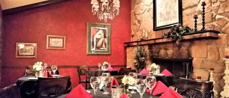 A dining area with red walls, a stone fireplace, and framed artwork.