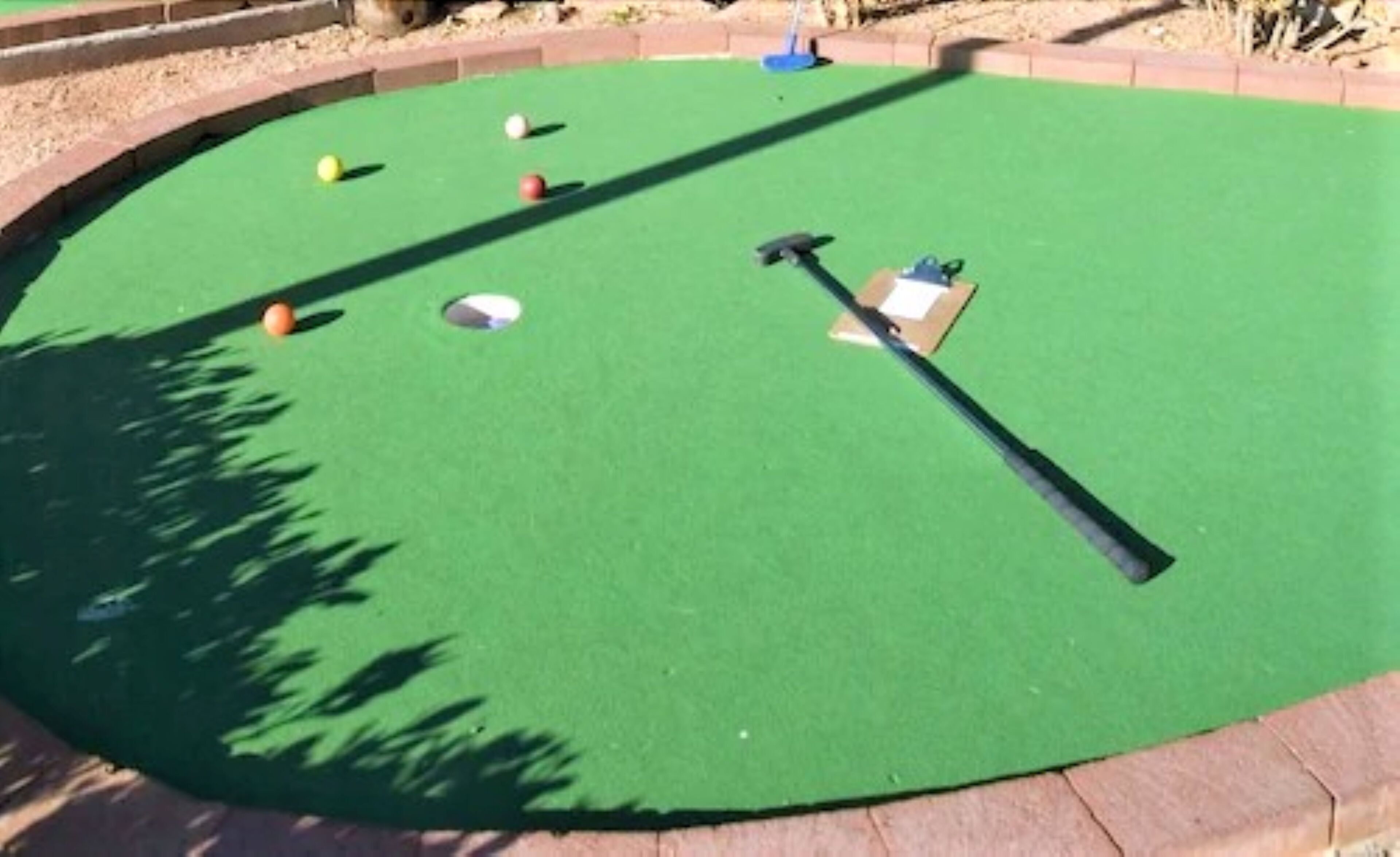 A miniature golf course with a green playing surface, a putter, and several golf balls.