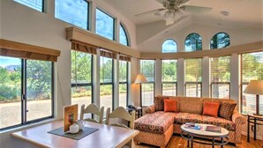 Une pièce spacieuse dotée d’une grande fenêtre, d’un ventilateur de plafond et d’un canapé agrémenté de coussins à motifs.