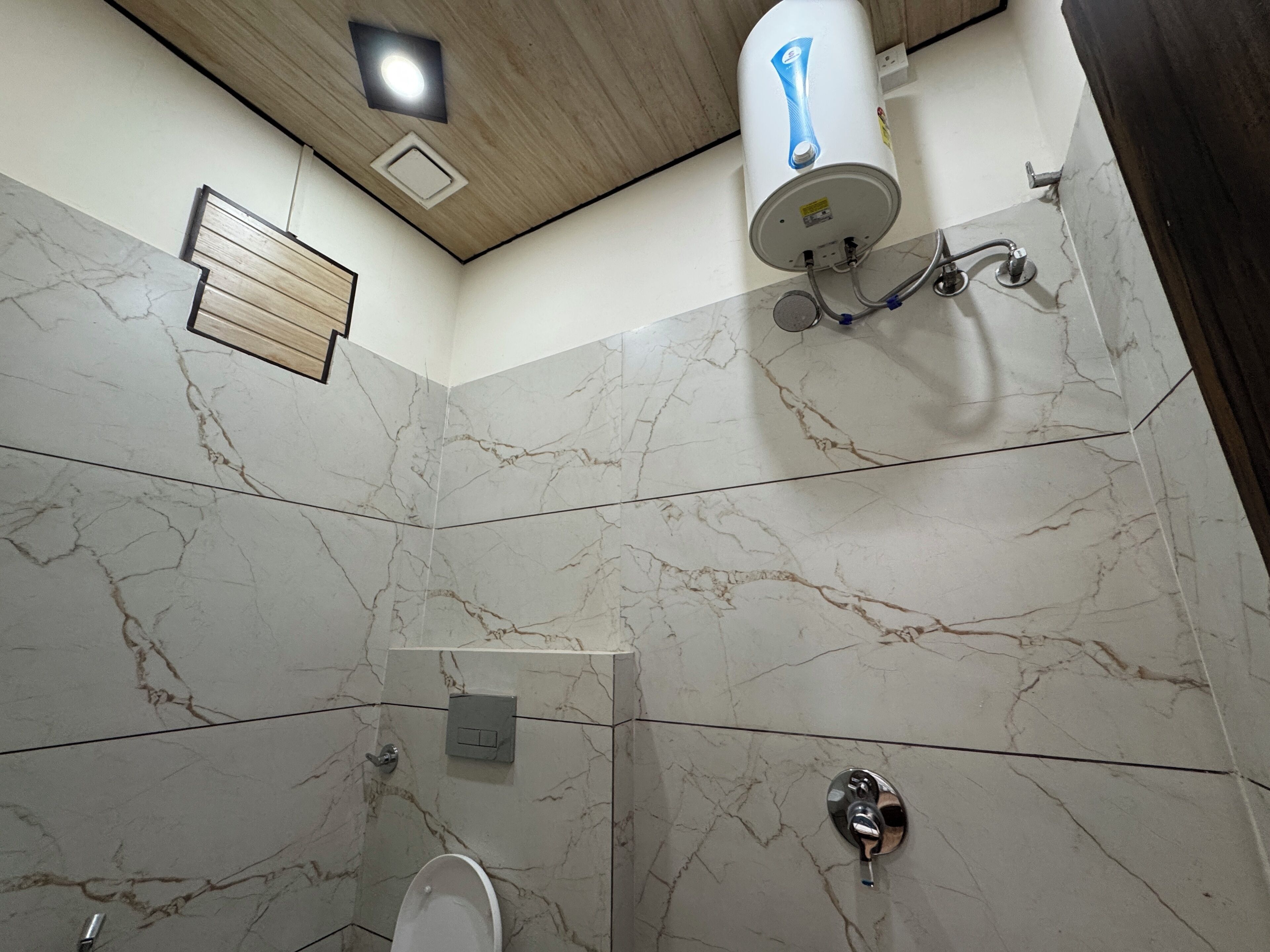 A bathroom with marble walls, a toilet, a shower, and a water heater.
