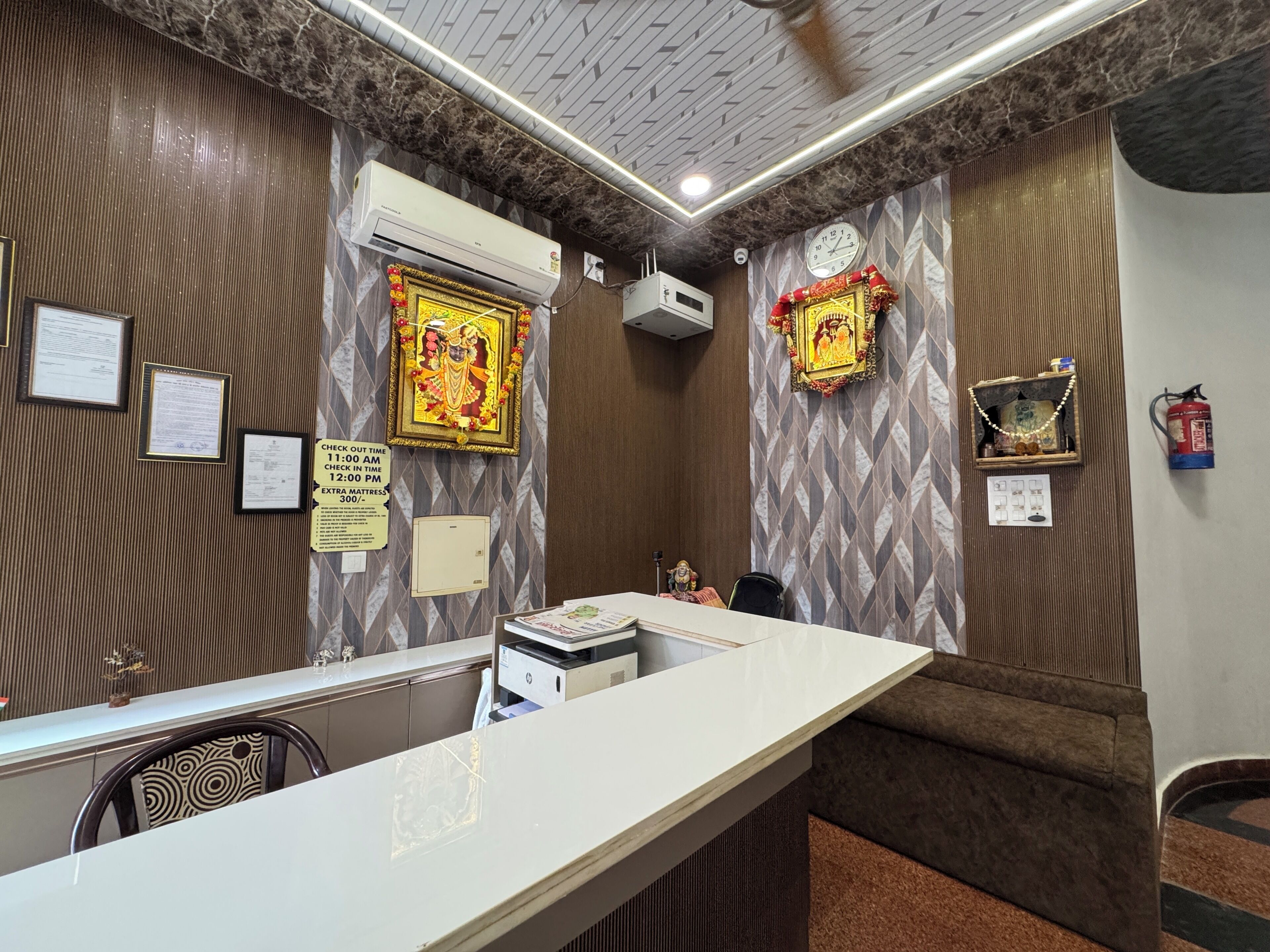 A hotel reception area with a marble counter, framed certificates, a clock, and a fire extinguisher.