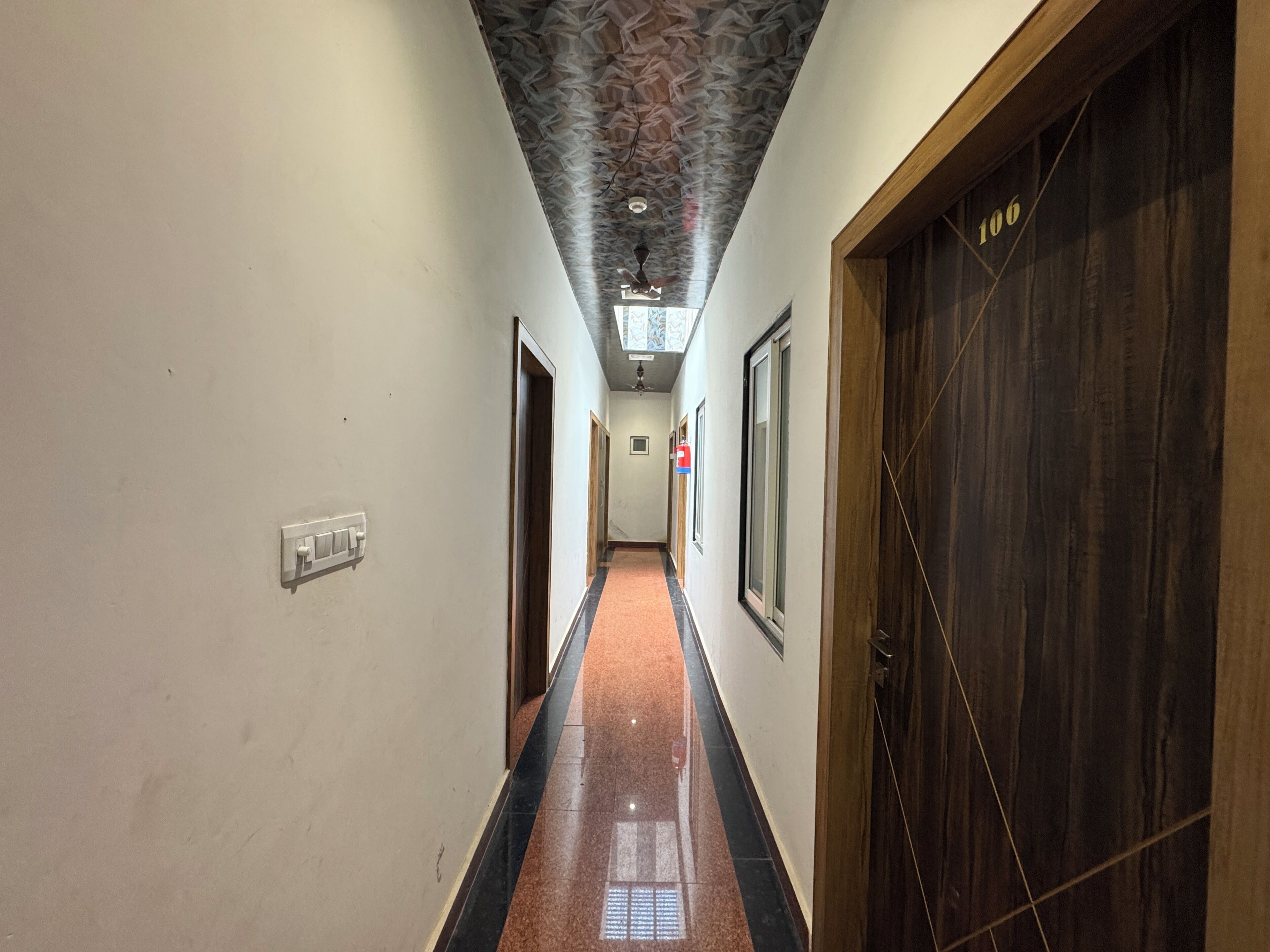 A hallway with a patterned ceiling, a fire extinguisher, and a door marked with the number 106.