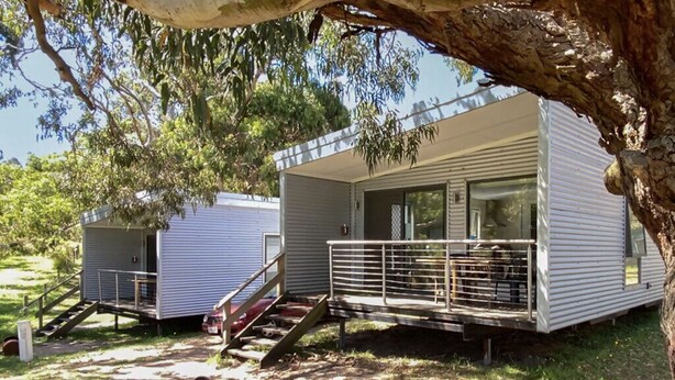Una casa móvil con balcón, una escalera que lleva a la entrada y un árbol en primer plano.